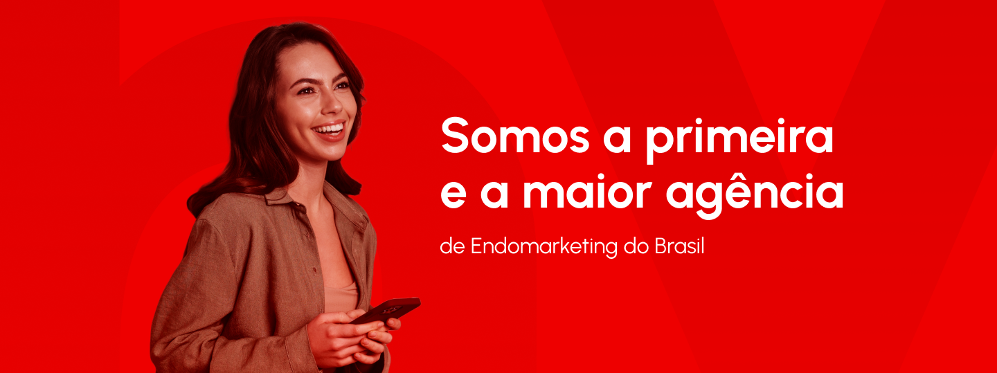 Mulher sorrindo e segurando um celular em frente a um fundo vermelho. Texto na imagem: 'Somos a primeira, e a maior agência de Endomarketing do Brasil'."